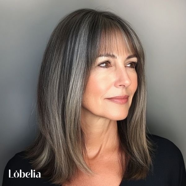 Woman over 60 with shoulder-length hair and blunt bangs, combining sharp bangs with a soft cut for a bold, stylish, and sophisticated look